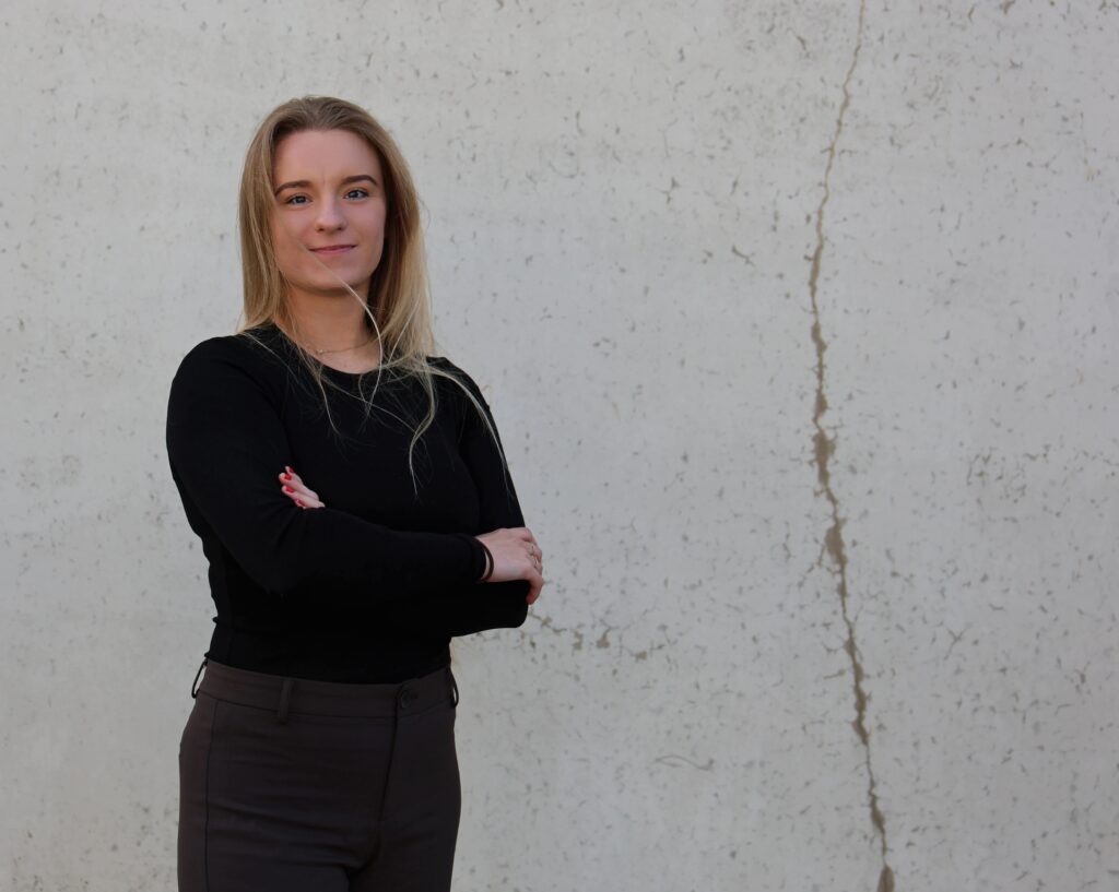 Team member Austeja from TRAVIS Road Services standing with arms crossed against a neutral background