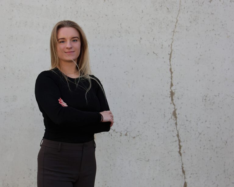 Team member Austeja from TRAVIS Road Services standing with arms crossed against a neutral background